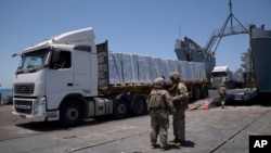 امریکی فوجی امریکی تعمیر کردہ گھاٹ پرانسانی ہمدردی سے لدے ٹرکوں کے پاس کھڑے ہیں ،جس کے بعد امداد کو غزہ کے ساحلی بیچ تک پہنچایا جائے گا۔ فوٹو اے پی 25 جون 2024 