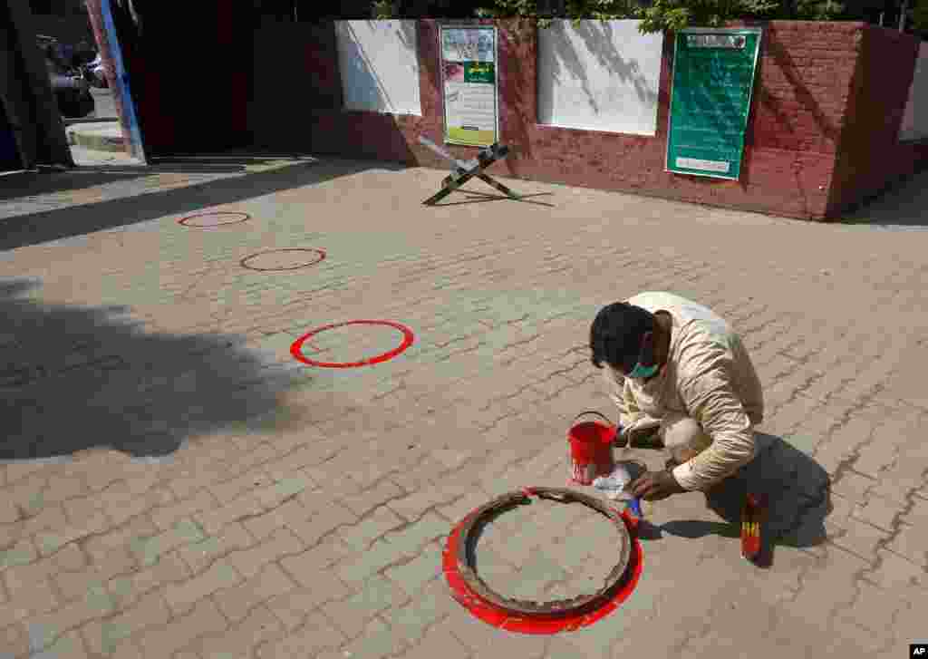 A worker paints circles for social distance at an entry gate of a school as preparation for reopening of educational institutions that were closed in March are finalized, in Lahore, Pakistan.