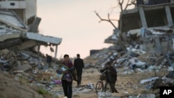 Orang-orang Palestina berjalan di sebuah jalan di Gaza City yang dipenuhi puing-puing dari gedung-gedung yang hancur akibat serangan darat dan udara Israel melawan Hamas, 4 Februari 2025. (Foto: Abdel Kareem Hana/AP Photo)