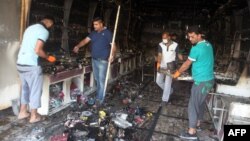 Iraqi men clear up a burned shop in Baghdad following two car bombs that were set off in mostly Shi'ite neighborhoods of the Iraqi capital, July 22, 2015.