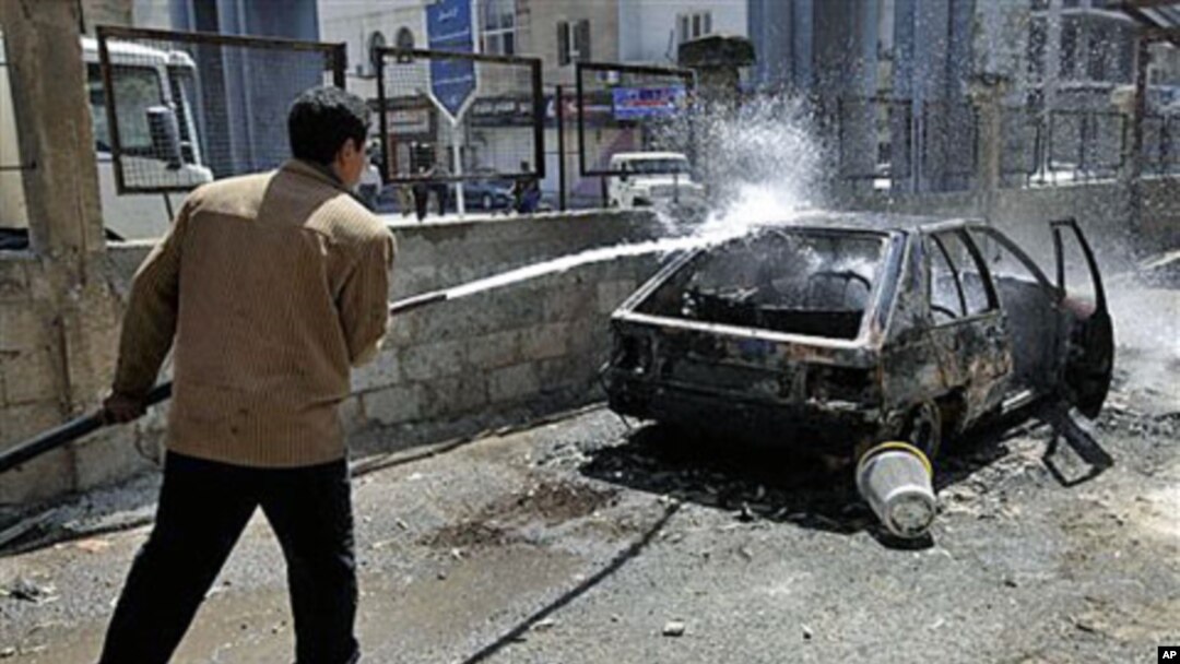 A Syrian municipality worker sprays water at a burnt car that was set on fire by Syrian anti-government protesters, in the southern city of Deraa, Syria, March 21, 2011