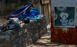 An Indian man sleeps next to a sign urging people to stay at home as a precaution against coronavirus in the premises of a hospital in Hyderabad, India, April 29, 2021.