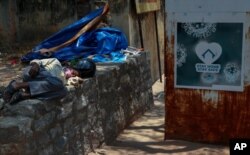 An Indian man sleeps next to a sign urging people to stay at home as a precaution against coronavirus in the premises of a hospital in Hyderabad, India, April 29, 2021.