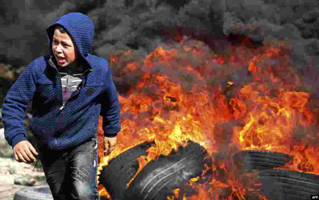 A Palestinian boy runs away from flaming tires during a weekly demonstration against the expropriation of Palestinian land by Israel, in the village of Kfar Qaddum, near Nablus in the occupied West Bank.