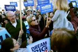 Democratic presidential candidate Sen. Elizabeth Warren, D-Mass., greets a young supporter as she walks from her home with husband Bruce Mann, left, to the nearby polling location to vote on March 3, 2020, in Cambridge, Mass.