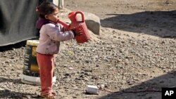 FILE - A girl drinks water in the street outside her tent at a camp for internally displaced people in western Baghdad, Iraq, Feb. 1, 2018. 