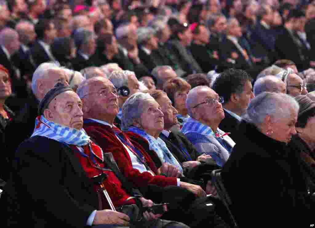 Holocaust survivors watch suspended screens in a tent raised at the entrance of the Birkenau Nazi death camp in Oswiecim, Poland during the official remembrance ceremony, Jan. 27, 2015.