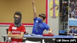 In this July 14, 2020, file photo, amid concerns of the spread of COVID-19, Aiden Trabucco, right, wears a mask as he raises his hand to answer a question behind Anthony Gonzales during a summer STEM camp at Wylie High School in Wylie, Texas.