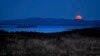 The nearly-full moon sets at dawn behind the Camden Hills in this view looking west across Penobscot Bay, near Camden, Maine.