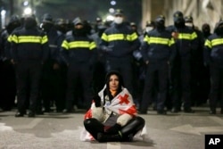 A demonstrator draped in a Georgian national flag sits in front of police outside the parliament building as protests continue against the government's decision to suspend negotiations on joining the European Union in Tbilisi, Georgia, Dec. 2, 2024.