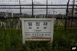 Tanda arah yang menunjukkan jarak ke Kaesong dan Seoul di Korea Utara di depan pagar yang dihiasi pita bertuliskan pesan yang mengharapkan penyatuan kembali kedua Korea di Paviliun Imjingak di Paju, Korea Selatan, 25 Mei 2024. (Jae C. Hong/AP)