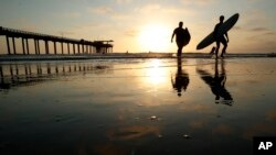 Surfers leave the water next to Scripps Pier, Aug. 2, 2018, in San Diego. A recent measurement of seawater temperature off Scripps Pier broke a record — it reached 79.5 degrees Fahrenheit on Aug. 9.