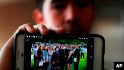 In this April 10, 2018, photo, Amos Cao, son of Chinese Rev. John Sanqiang Cao, holds a family photo showing his father, far right, in Ann Arbor, Mich. 
