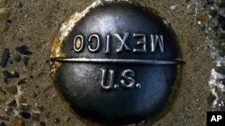 FILE - A marker embedded in the pavement marks the imaginary line between the United States and Mexico at the San Ysidro border checkpoint between San Diego, Calif., and Tijuana, Mexico, April 10, 2000. 