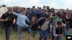 FILE - In this image taken from TV, Hungarian camerawoman Petra Laszlo, center left in blue, kicks out at a young migrant who had just crossed the border from Serbia near Roszke, Hungary, Sept. 8, 2015. 