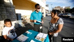 FILE - Jaime Corona, patient care coordinator at AltaMed, speaks to a woman during a community outreach on Obamacare in Los Angeles, California.