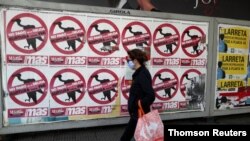 FILE - A pedestrian wearing a face mask as a preventive measure against the coronavirus walks past posters on the street that read 'No to the payment of the debt. Break with the IMF' in Buenos Aires, Argentina, May 27, 2020.