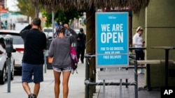 FILE - Pedestrains walk past an "open sign" at a restaurant in Long Beach, California, May 12, 2020.