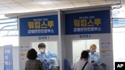FILE - Medical workers in a booth take samples from people for COVID-19 tests at a makeshift clinic in Seoul, South Korea, Aug. 20, 2020.