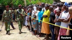 Kenyan police men walk past members of the public standing behind the cordoned off area outside the church where gunmen attacked worshippers attending a church service in Mombasa, March 23, 2014.