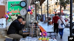 Salah Nasab, a Lebanese street vendor who also sells and repairs clocks, sits next of two clocks that show different times in Lebanon, in the southern port city of Sidon, Lebanon, March 27, 2023. 