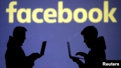 FILE - Silhouettes of laptop users are seen next to a screen projection of Facebook logo in this picture illustration taken March 28, 2018. 