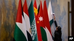 FILE - A staff member wipes on national flags from left, Palestinians, Egypt, Saudi Arabia, China, Jordan, Indonesia and Organization of Islamic Cooperation before a round table meeting with Chinese Foreign Minister Wang Yi in Beijing, Nov. 20, 2023. 