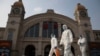 FILE - Workers in protective suits walk past the Hankou railway station on the eve of its resuming outbound traffic in Wuhan in central China's Hubei province, April 7, 2020. 