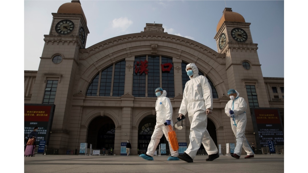 FILE - Workers in protective suits walk past the Hankou railway station on the eve of its resuming outbound traffic in Wuhan in central China's Hubei province, April 7, 2020.