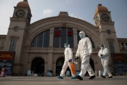 FILE - Workers in protective suits walk past the Hankou railway station on the eve of its resuming outbound traffic in Wuhan in central China's Hubei province, April 7, 2020.