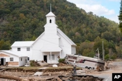 In the aftermath of Hurricane Helene, Dominick Gucciardo walks by a bus pushed by floodwaters against Laurel Branch Baptist Church in Pensacola, North Carolina, Oct. 3, 2024.