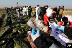 FILE - A rescue worker shows pictures of a girl recovered from a Ukrainian plane crash site in Shahedshahr, southwest of the capital Tehran, Iran.