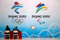 Staff members sit near a board with signs of the 2022 Olympic Winter Games, at the National Aquatics Center, known colloquially as the "Ice Cube", in Beijing, China, April 1, 2021.