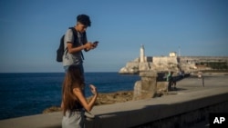 A youth uses his smartphone as he and a friend walk along the Malecon seawall in Havana, Cuba, Friday, Nov. 25, 2022. 