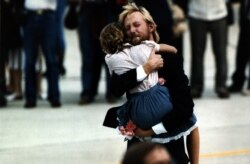 FILE - While holding carnations he carried off the plane, former hostage Victor Amburgy hugs an unidentified girl upon arrival at Andrews Air Force Base, July 2, 1985. Thirty former hostages from TWA flight 847 were greeted by President Reagan.