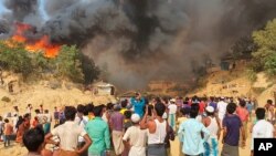 Rohingya refugees watch smoke rising from a fire at the Rohingya refugee camp in Balukhali, southern Bangladesh, March 22, 2021.