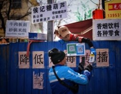 FILE - A deliveryman scans a QR code from an employee of a restaurant as he picks up food over barriers set up to block an entrance to a food street, following an outbreak of the novel coronavirus, in Jinan, Shandong province, China, March 15, 2020.