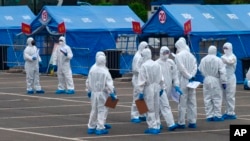 Para pekerja pemerintah berdiri di luar tenda biru yang digunakan untuk mengoordinasikan transportasi para pelancong dari Wuhan ke lokasi karantina yang telah ditentukan di Beijing, 15 April 2020. (Foto: AP)