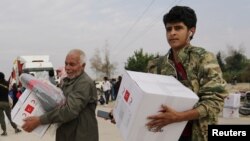 FILE - People hold boxes of aid donated by the Turkish Red Crescent in the border town of Tal Abyad, Syria, Oct. 19, 2019.