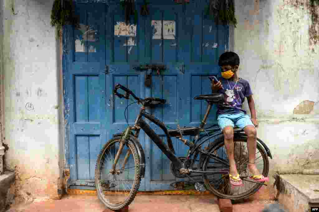 Kijana akiwa amevaa barakoa amekaa mbele ya duka akitumia simu wakati maduka yalipotakiwa kufungwa ili kudhibiti maambukizi ya COVID-19 huko Hyderabad Julai 16, 2020.(Photo by NOAH SEELAM / AFP)