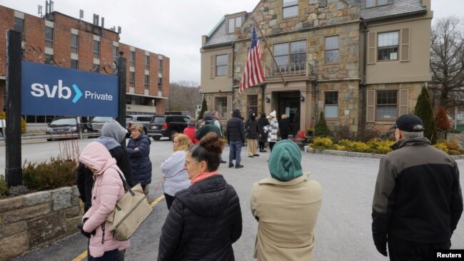 Customers wait in line outside a branch of the Silicon Valley Bank in Wellesley, Massachusetts, March 13, 2023.