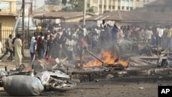 People gather at the site of a bomb explosion at a road in Kaduna, Nigeria on Sunday, April 8, 2012.