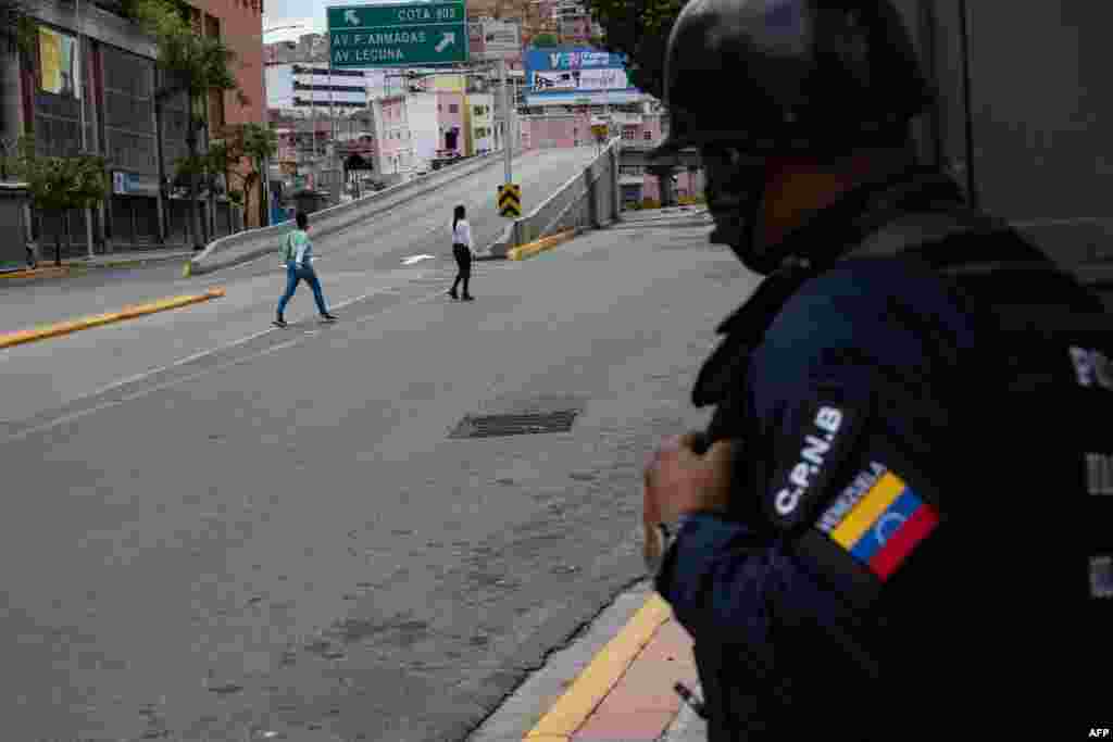 Un miembro de la Polic&#237;a Nacional Bolivariana observa a dos mujeres cruzar durante enfrentamiento. A pesar de los reportes extraoficial, todav&#237;a no hay informaci&#243;n oficial de v&#237;ctimas o heridos por la situaci&#243;n. Junio, 8 2021. Foto: Yuri Cortez - AFP. 