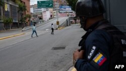 Un miembro de la Policía Nacional Bolivariana observa a dos mujeres cruzar una avenida vacía durante enfrentamientos entre policías y presuntos integrantes de una banda criminal en los alrededores del barrio La Cota 905 de Caracas. Julio 8, 2021.