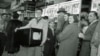 FILE - Phil Bustos of Trinidad, Colorado, displays a television set he bought for $29 at a Washington's Birthday sale in Washington, D.C., Feb. 22, 1954. Other bargain hunters waited to get into the packed store during the annual holiday sale.