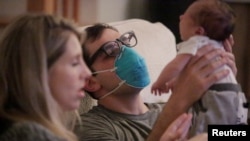 Emergency medicine physician Thomas Krajewski wears a mask as he holds his baby Cal with his wife Genevieve after finishing his shift amid an outbreak of coronavirus disease (COVID-19) in New Orleans, Louisiana, U.S., March 27, 2020. (REUTERS/Kathleen Flynn)