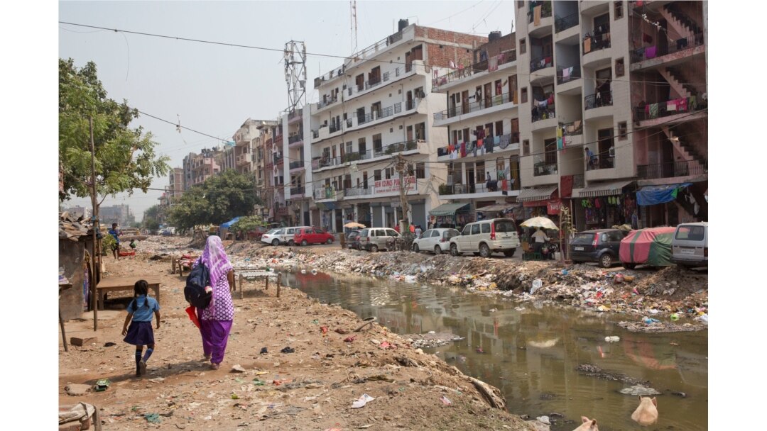 FILE - An Indian woman walks with a child along an open drain filled with plastic and stagnant water, which act as a breeding ground for mosquitoes in New Delhi, India, Sept. 20, 2016.
