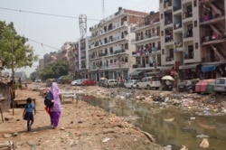 FILE - An Indian woman walks with a child along an open drain filled with plastic and stagnant water, which act as a breeding ground for mosquitoes in New Delhi, India, Sept. 20, 2016.