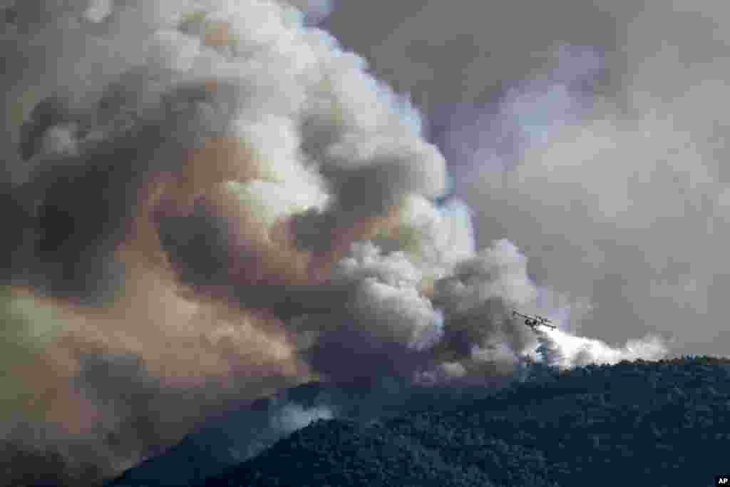 A firefighting plane drops water on a hill side, near the seaside area Kechries, near Corinth, Greece, on Wednesday, July 22, 2020.