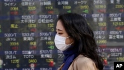 A woman walks by an electronic stock board of a securities firm in Tokyo, Wednesday, March 18, 2020.